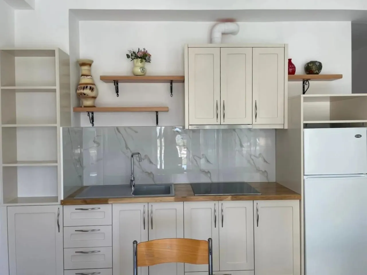 White apartment kitchen with a fridge, hob and a bowl of fruit on the table